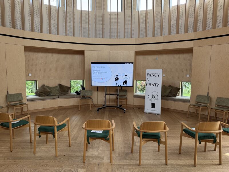 A circle of chairs set out for a Men Who Talk workshop in a light, wood panelled meeting room.